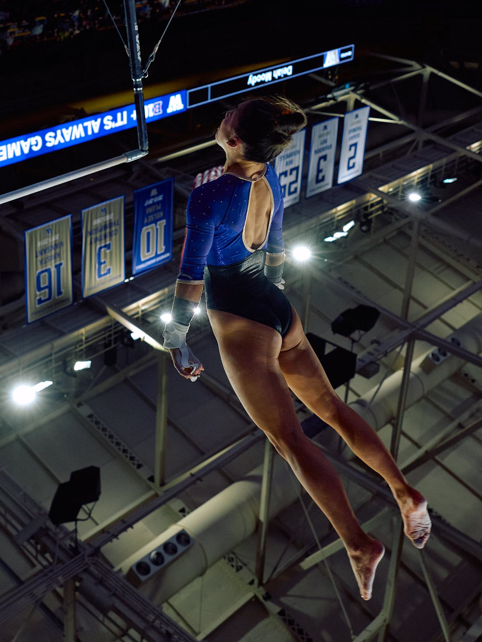 Olivia Oppegard of the Washington women's gymnastics team executing a precise gymnastics routine. Her body is fully extended in mid-air, showcasing her form and control. The indoor setting at Alaska Airlines Arena in Seattle, Washington, adds to the competitive atmosphere.